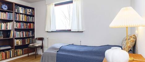 Une chambre à coucher avec un lit, une bibliothèque, une chaise, une fenêtre et une lampe.