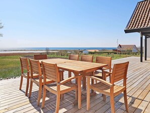 En træterrasse med et bord og stole med udsigt over en strand.