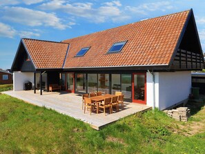 Et moderne hus med skråt tag, store glasruder og en træterrasse.