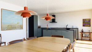 A modern kitchen with a dining area, featuring pendant lights, a large painting, and a view of the outdoors. - 10 Person Holiday Home in Assens (Assens)