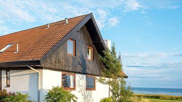 A two-story house with a sloped roof, a visible chimney, and a view of the sea.