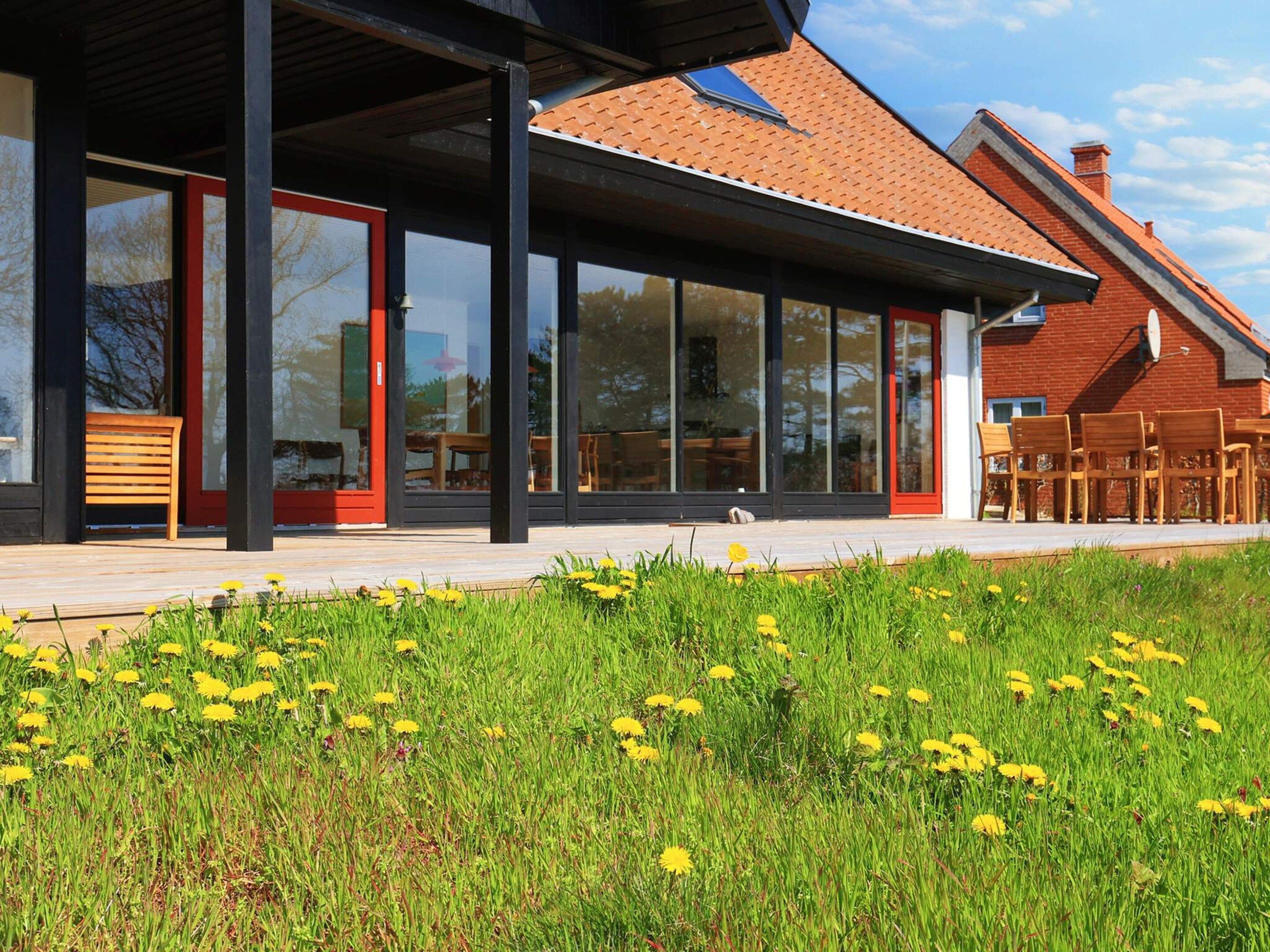A modern building with large windows, a covered patio area, and a garden with yellow flowers.