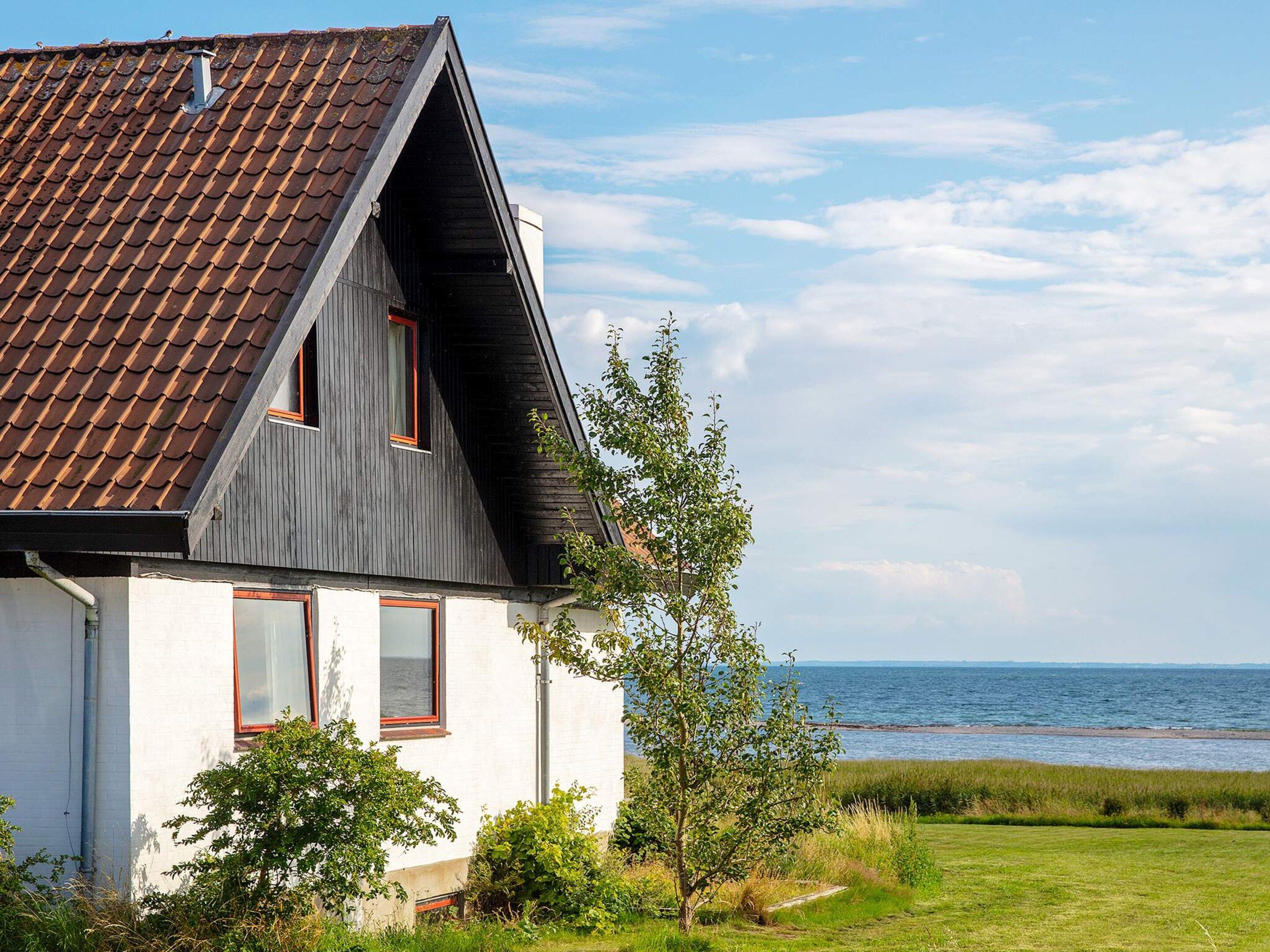 A house with a sloped roof, two windows with red frames, and a view of the sea.