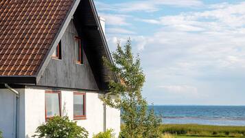 A house with a sloped roof, two windows with red frames, and a view of the sea.