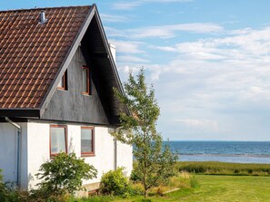 A house with a sloped roof, two windows with red frames, and a view of the sea. - 10 Person Holiday Home in Assens (Assens)