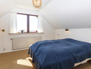Et soveværelse med seng, et vindue med gardiner, en radiator og en lampe.