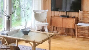 A living room with a large TV, a white chair, a wooden cabinet, and a glass table. - 7 Person Holiday Home in Sortland (Sortland)