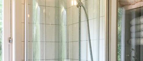 Une douche fermée par des parois en verre, dotée d’un pommeau de douche à main et d’un robinet fixé au mur.