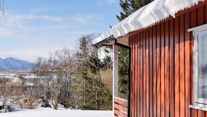 A cabin with a snow-covered roof and a view of a snowy landscape and mountains in the background. - 7 Person Holiday Home in Sortland (Sortland)