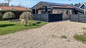 A modern house with a gravel driveway, a fenced yard, and a flag on a pole. - 4 Person Holiday Home in Hemmet (Hemmet)
