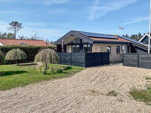 A modern house with a gravel driveway, a fenced yard, and a flag on a pole. - 4 Person Holiday Home in Hemmet (Hemmet)
