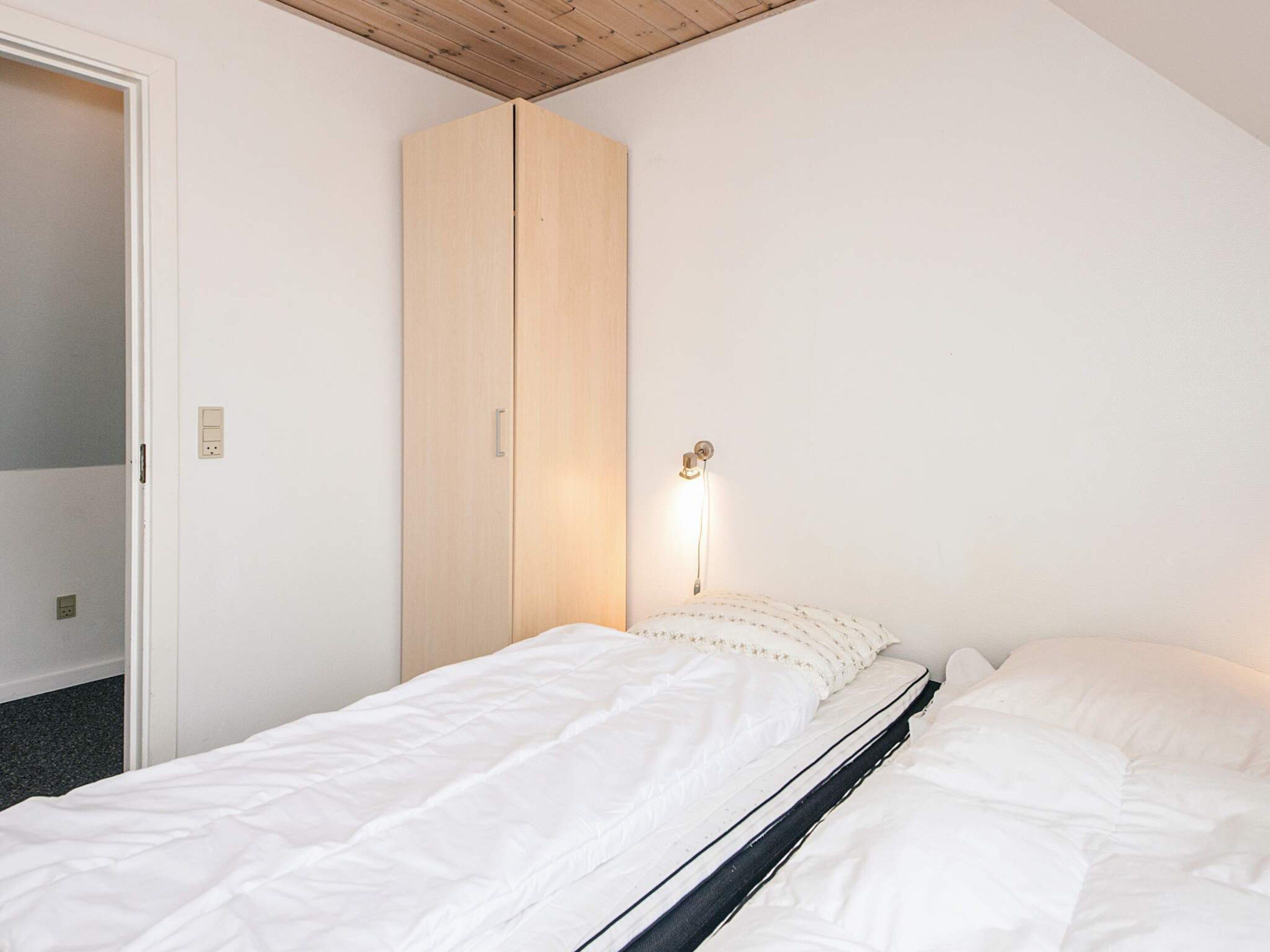 A single bed with white bedding, a wooden wardrobe, and a wall-mounted light fixture.