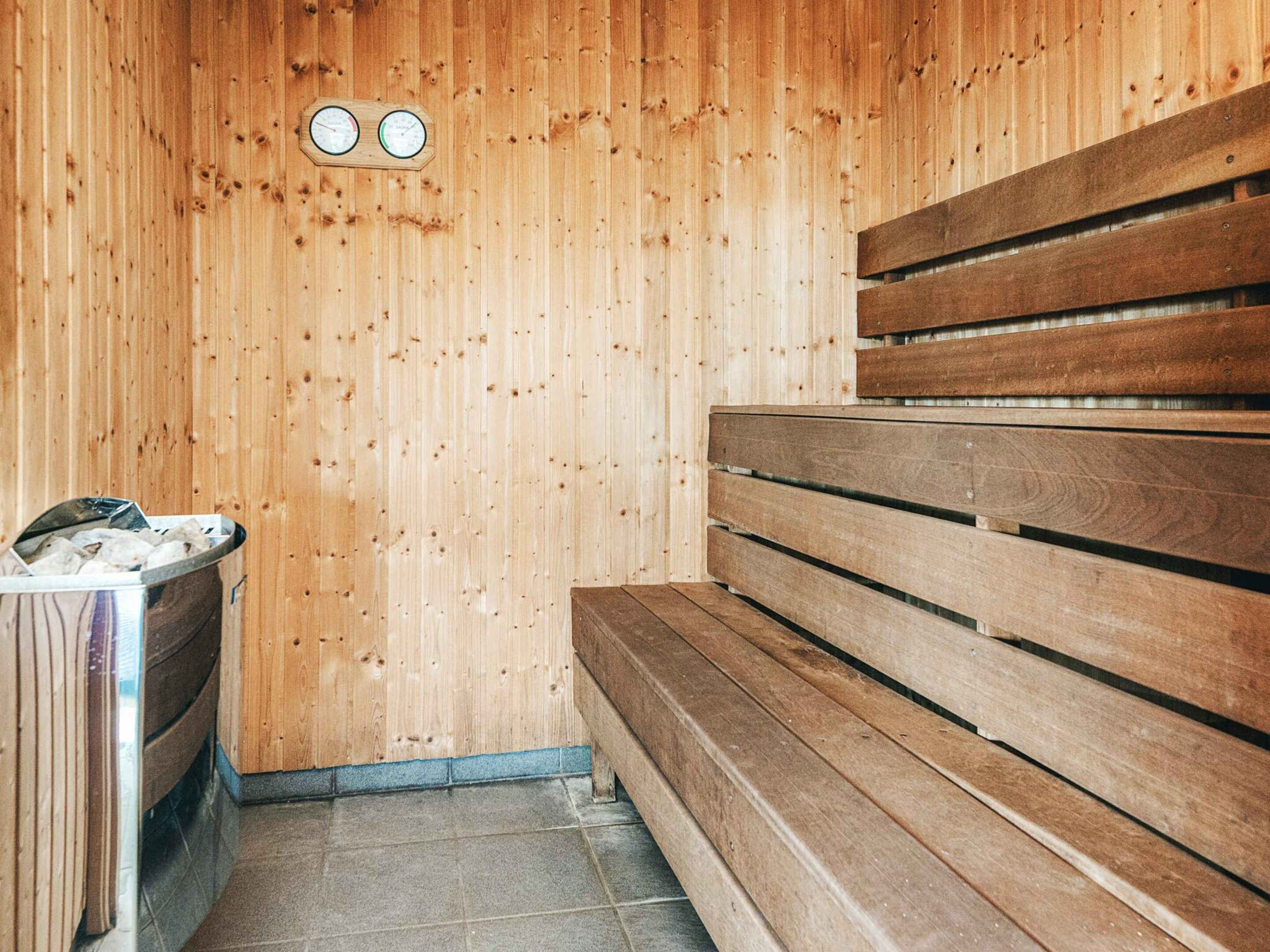 A sauna with wooden benches and a metal container, likely for towels or bath items.