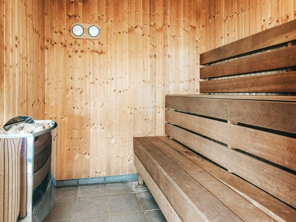 A sauna with wooden benches and a metal container, likely for towels or bath items.