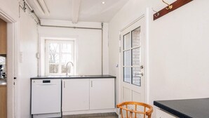Eine Küche mit weißen Schränken, einem Geschirrspüler, einem Fenster und einem Holzbstuhl.