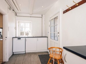 A kitchen with white cabinets, a dishwasher, a window, and a wooden chair.