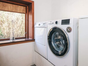 A front-loading washing machine with a 10-year warranty sticker, positioned next to a window with a wooden frame.