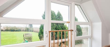 A room with a large skylight, a view of a green field, and a wooden bench outside.