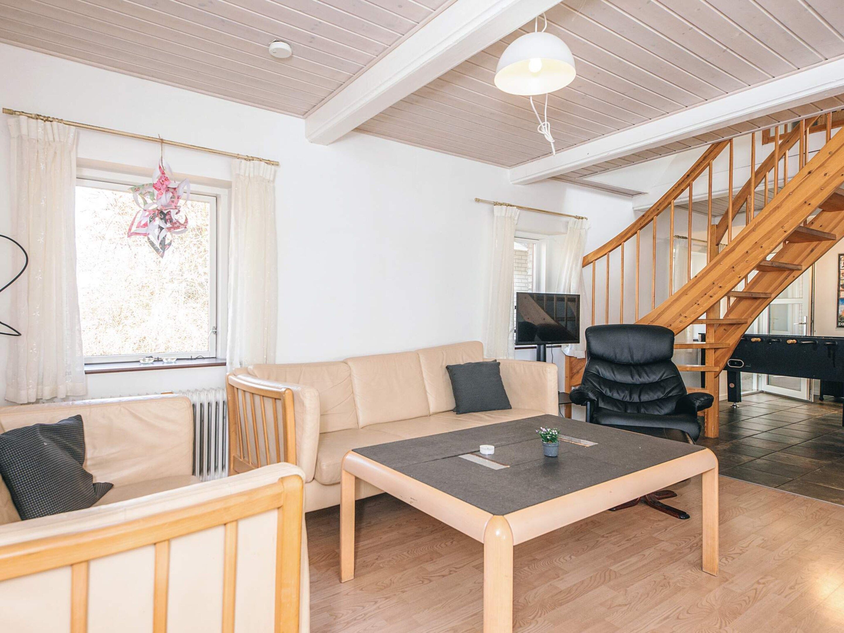 A living room with a sofa, a table, a chair, a staircase, and a television.