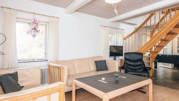 Uma sala de estar com sofá, mesa, cadeira, escada e televisão.