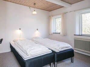A bedroom with two beds, a wooden ceiling, a window with curtains, and a radiator.