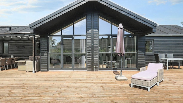 A modern house with a large glass facade, outdoor seating area, and a wooden deck. - 8 Person Holiday Home in Hals-by Traum (Hals)