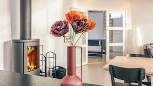 A modern interior with a wood-burning stove, a dining area, and a vase with flowers. - 8 Person Holiday Home in Hals-by Traum (Hals)