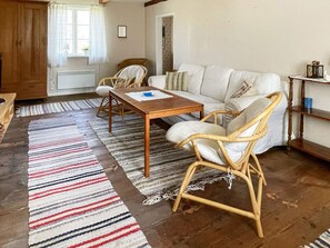 A cozy living room with a sofa, two wicker chairs, a wooden coffee table, and a striped rug.