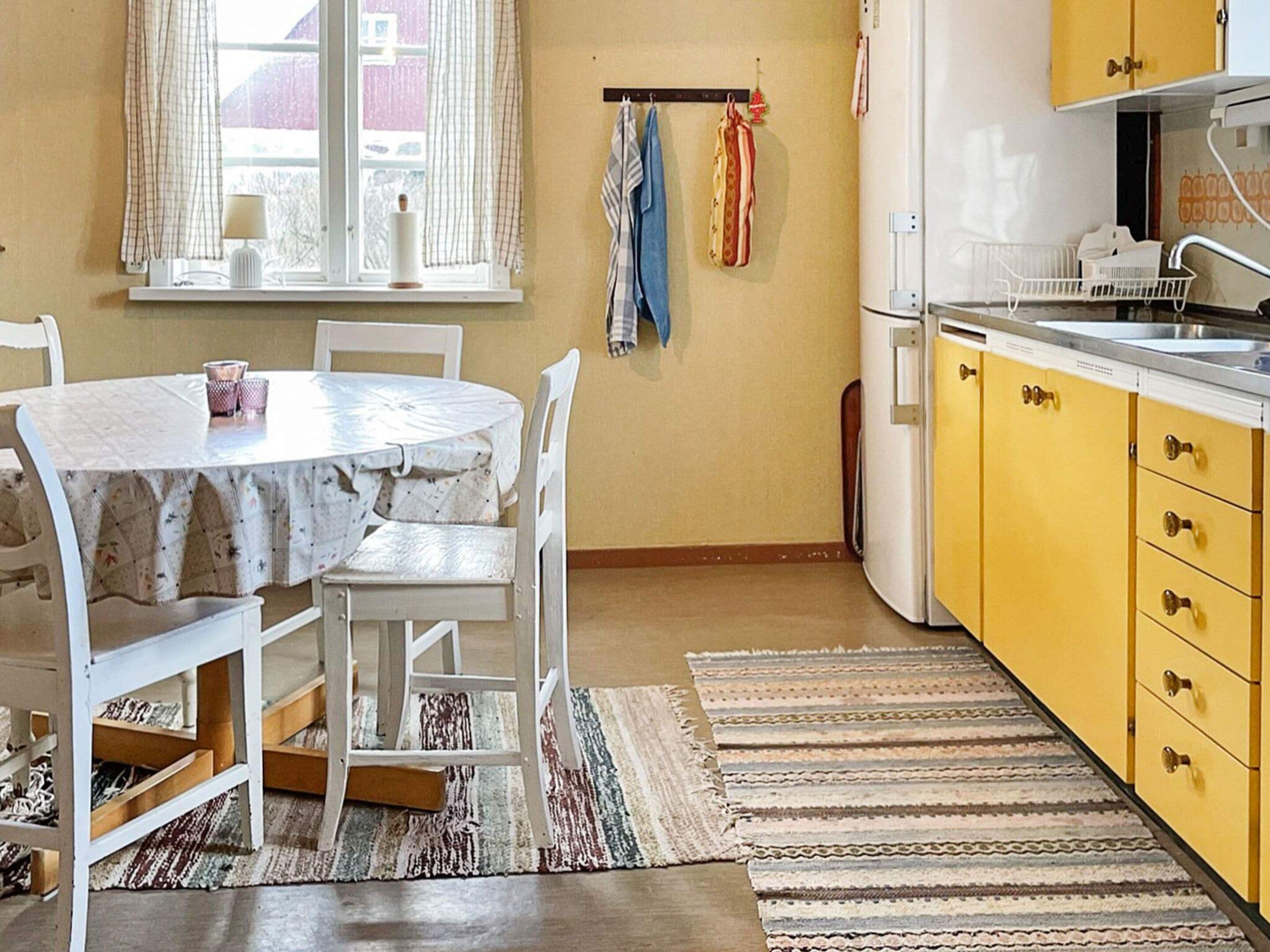 A kitchen with a round table, chairs, a refrigerator, and a window with curtains.