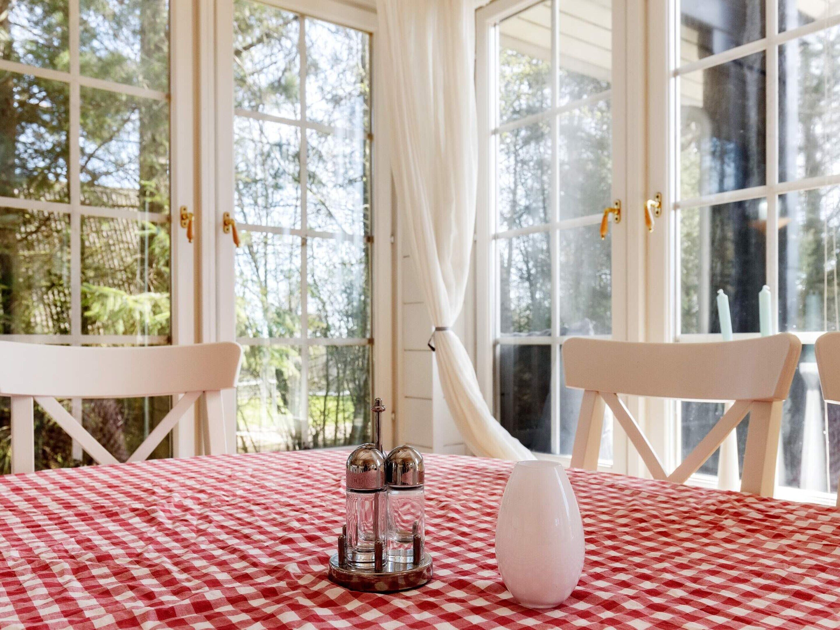 A room with a checkered tablecloth, two chairs, a salt and pepper set, and a vase.