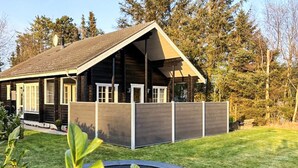 A log cabin with a fenced deck, surrounded by a well-maintained lawn and trees. - 7 Person Holiday Home in Logstor (Logstor)