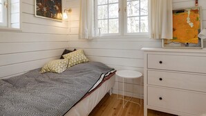 A single bed with a patterned bedspread, a bedside table, a dresser with drawers, a window with curtains, and a wall-mounted painting. - 7 Person Holiday Home in Logstor (Logstor)