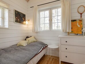 A single bed with a patterned bedspread, a bedside table, a dresser with drawers, a window with curtains, and a wall-mounted painting. - 7 Person Holiday Home in Logstor (Logstor)