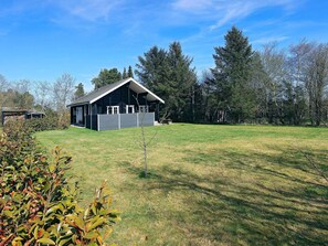 Ein Haus mit geneigtem Dach, einer überdachten Veranda und einem eingezäunten Garten.