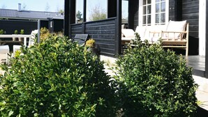 A covered outdoor seating area with a wooden deck, a white door, and a window. - 7 Person Holiday Home in Logstor (Logstor)