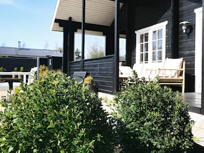 A covered outdoor seating area with a wooden deck, a white door, and a window.
