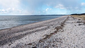 A wide beach with a pebbly shore and a calm sea under a cloudy sky. - 7 Person Holiday Home in Logstor (Logstor)