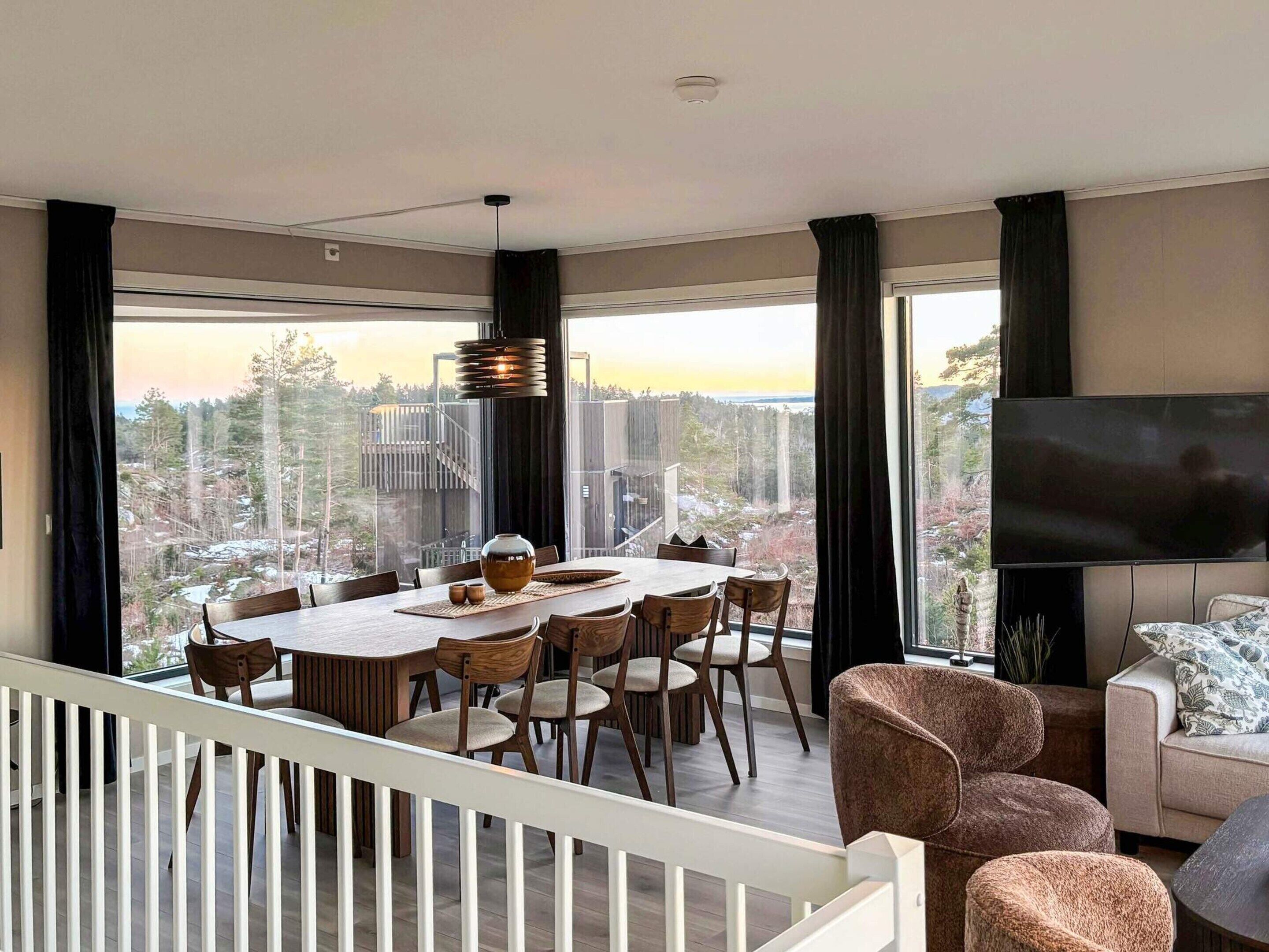Ein modernes Wohnzimmer mit Essbereich, großen Fenstern, einem Flachbildfernseher und einer Treppe.
