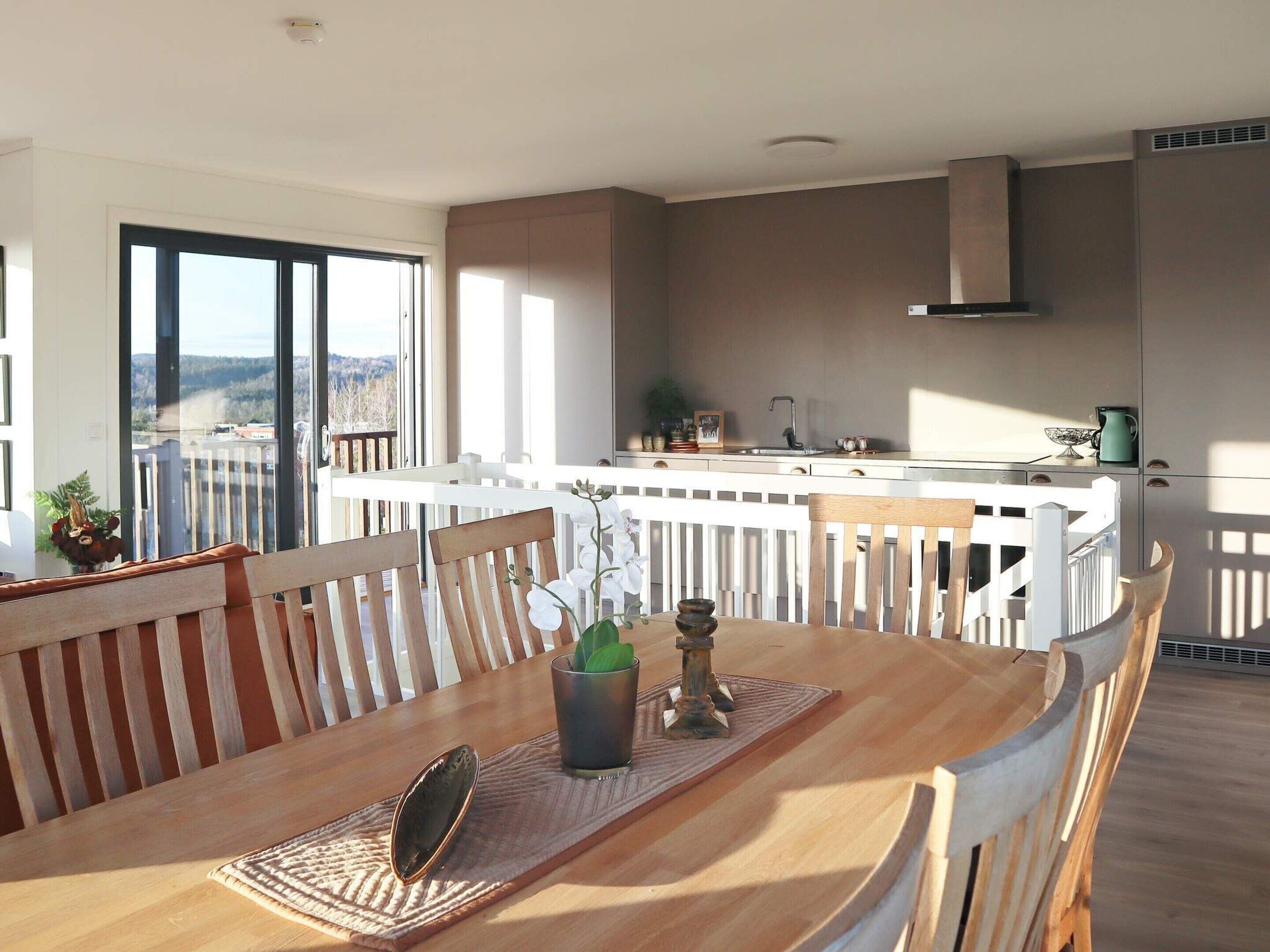 A dining area with a wooden table and chairs, a view of the cityscape through large windows, and a modern kitchen in the background.
