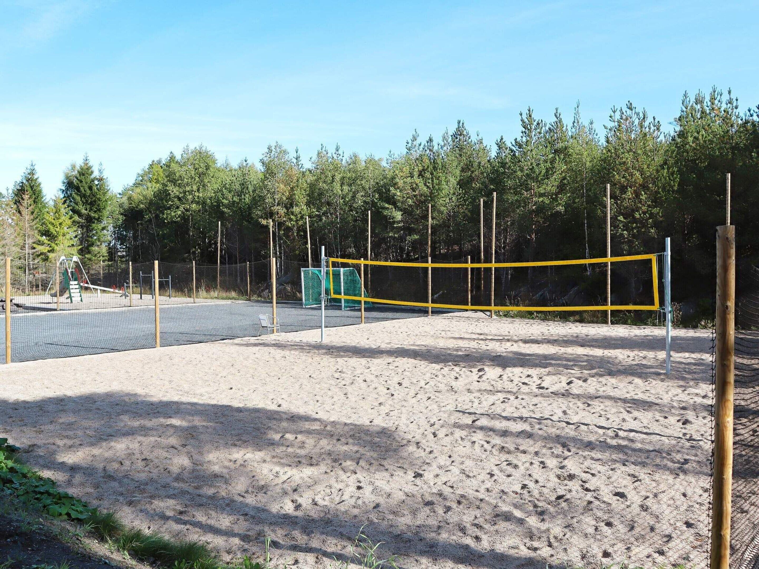 An outdoor volleyball court with a net, surrounded by trees and a sandy area.