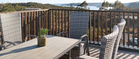 A deck with a table and chairs, overlooking a scenic view of a lake and forest.