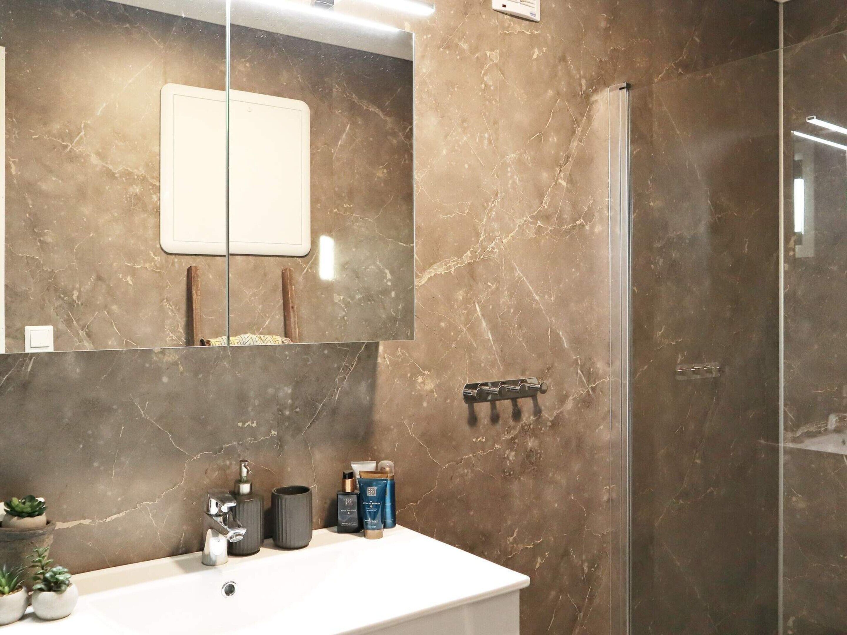 Une salle de bain avec un grand miroir, un lavabo blanc et une douche.