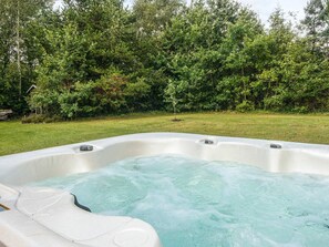 Un jacuzzi en un patio trasero con césped y follaje denso al fondo.