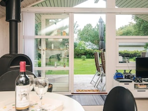 A cozy indoor dining area with a table set for two, a wine bottle, and a glass. A large window offers a view of a garden and a statue.