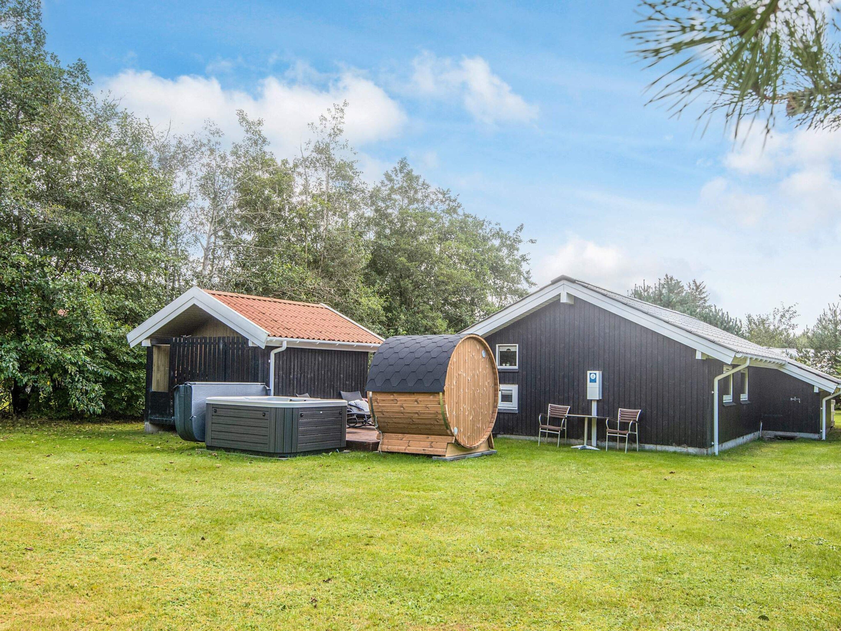A rustic barn with a large barrel, a small shed, and a grassy field.