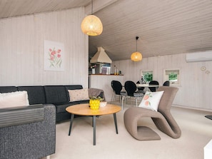 A modern living room with a sofa, a round coffee table, and a unique armchair. There is a dining area with chairs and a table in the background.