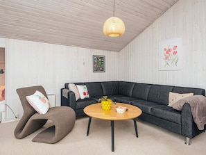 A modern living room with a dark grey sectional sofa, a brown armchair, a wooden coffee table, and a woven pendant light.