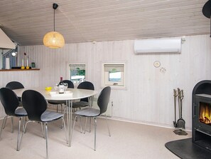 Un comedor con una mesa redonda, seis sillas, una lámpara colgante, una chimenea y un ventanal.