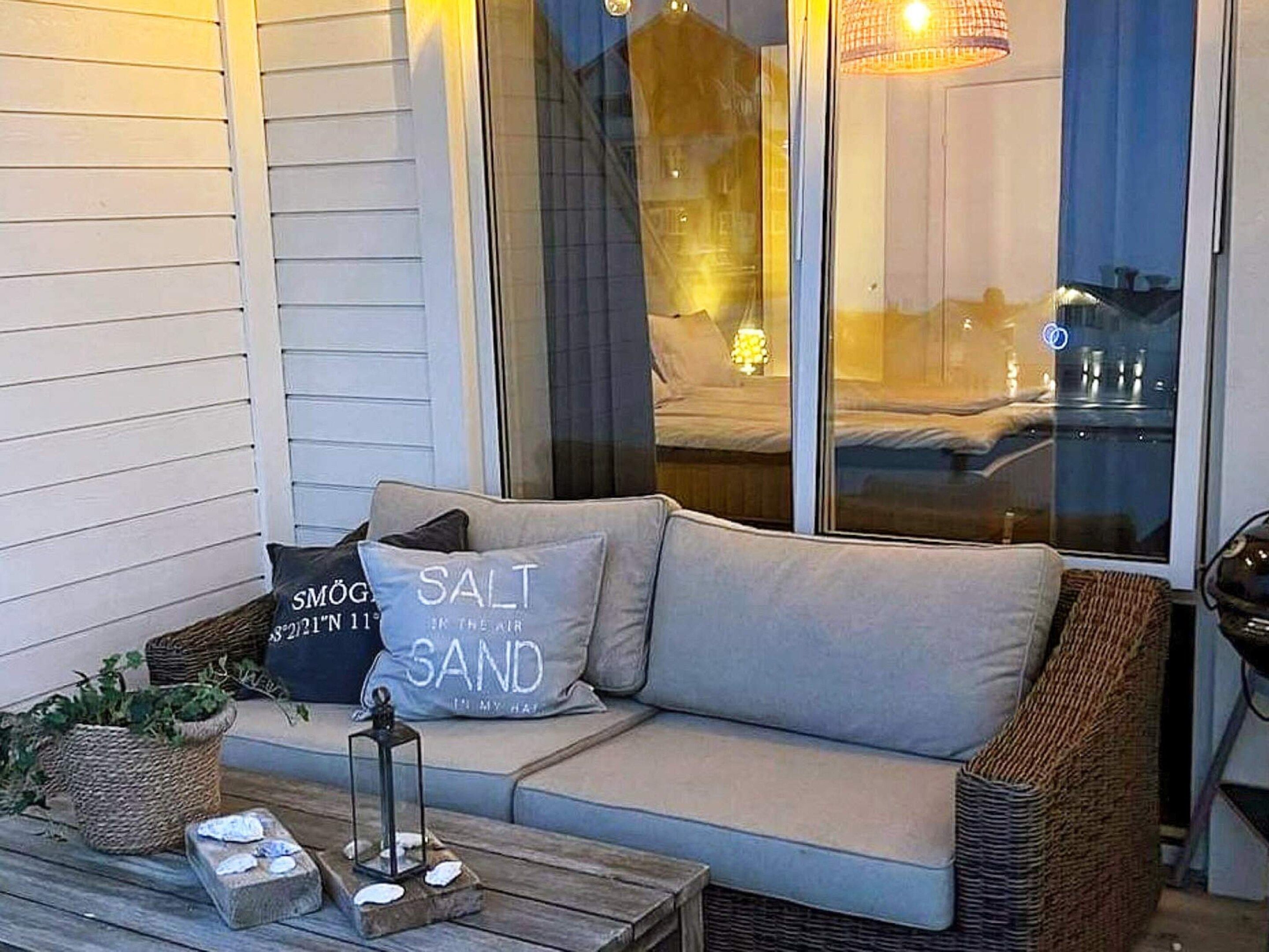 Een knus terras met een comfortabele bank, rieten meubels en een lantaarn op een houten tafel.