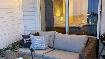 Een knus terras met een comfortabele bank, rieten meubels en een lantaarn op een houten tafel.